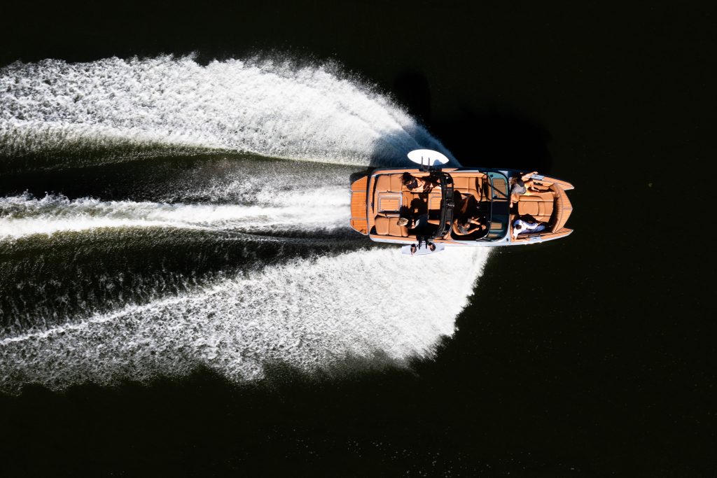 Aerial view of wakeboard boat with tan vinyl interior cruising on dark water with wake